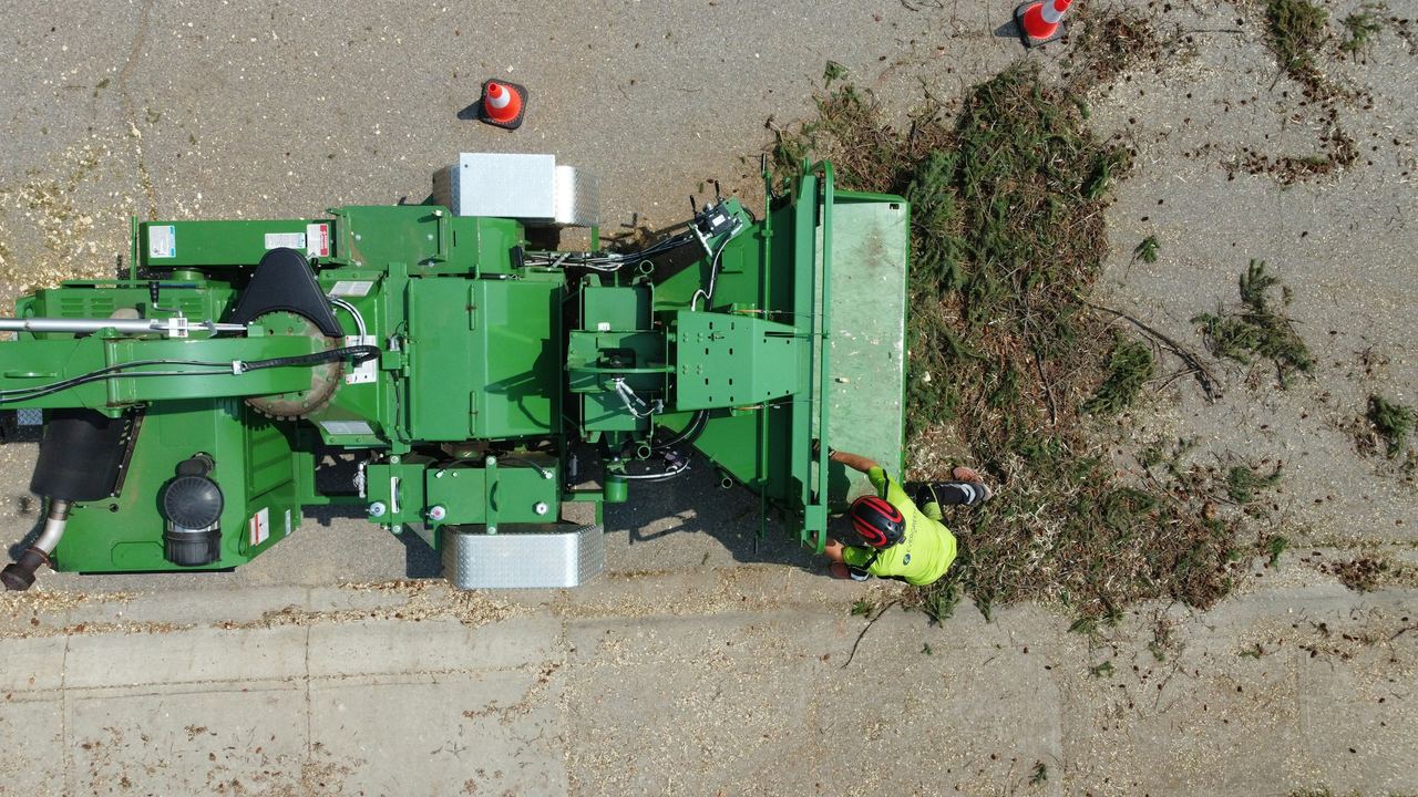 Aerial view of a wood chipper and brush pile during tree work on a paved driveway